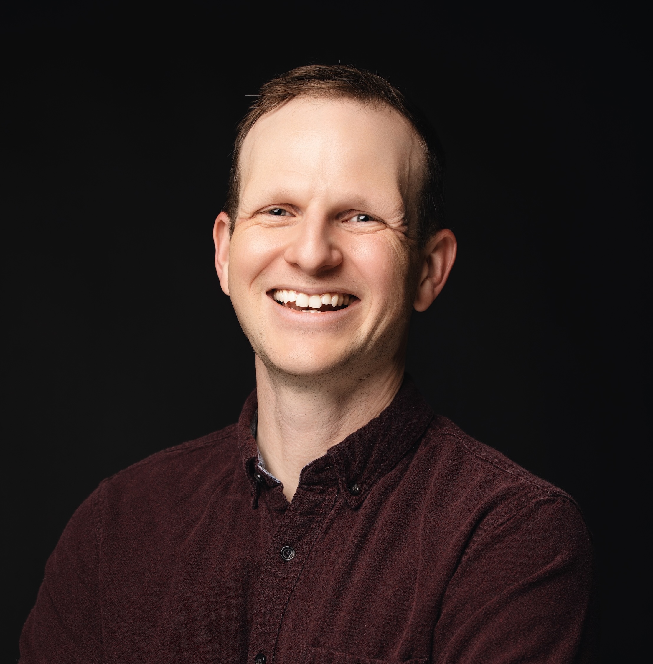 Headshot of Jake Mitchell, a white man wearing a burgundy shirt